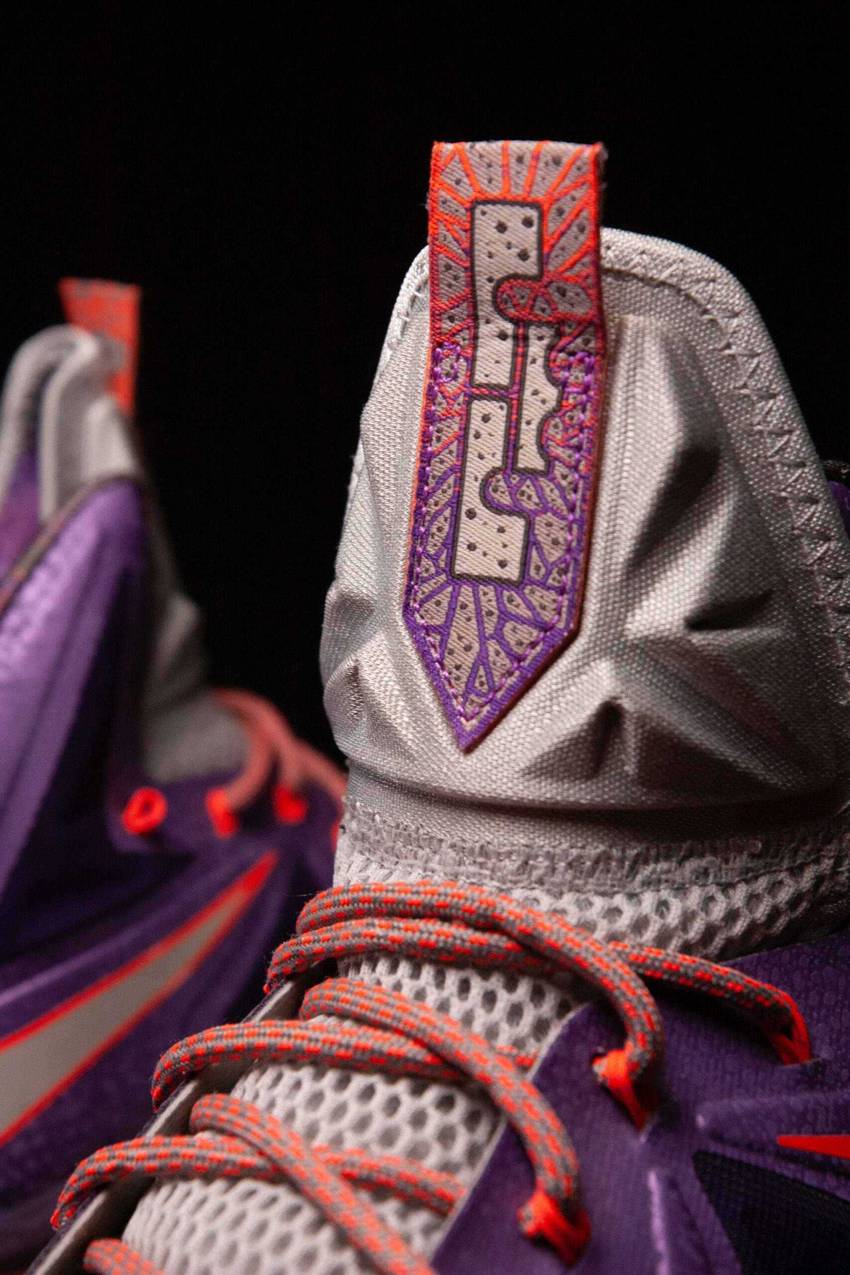 Close-up da lingueta do tênis Nike LeBron Witness com logo LBJ em roxo e laranja